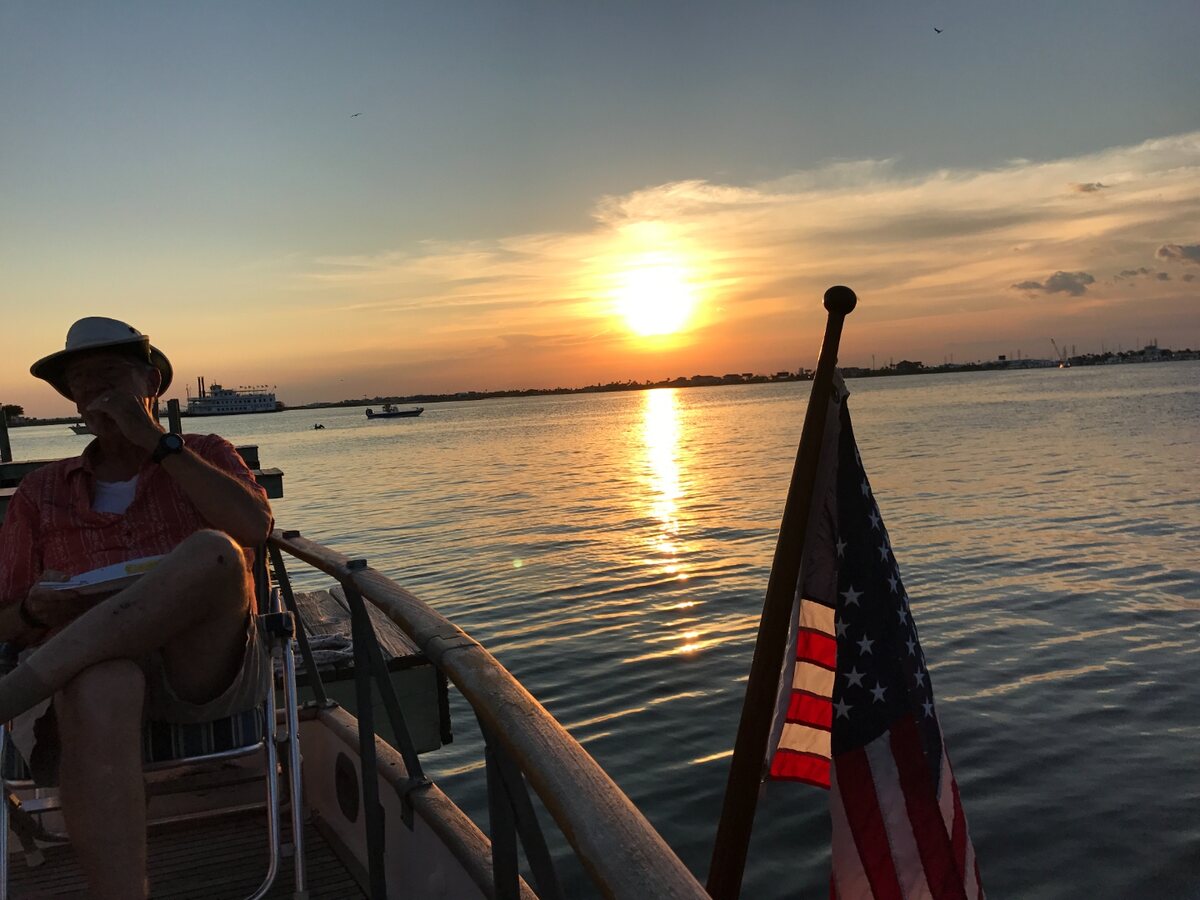 Sunset over Galveston Bay from a boat with an American flag in the foreground.